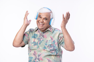 Senior man listening music over headphones and looking up against white background