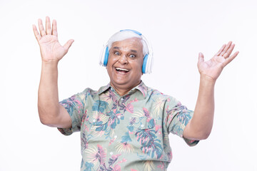 Senior man listening music over headphones and looking up against white background