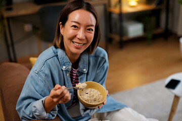 Smiling Asian woman eating healthy oatmeal for breakfast at home