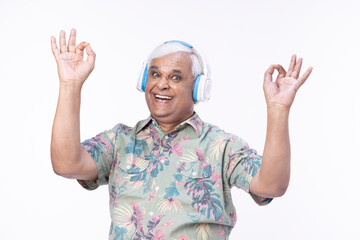 Senior man listening music over headphones and looking up against white background