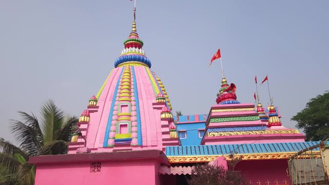 Vibrant pink Hindu temple with a beautifully decorated shikhara and fluttering flags stands against a clear blue sky, representing Indian religious architecture and spiritual culture.