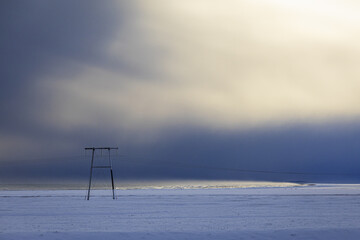 View of stark, snow-covered plains stretch under a dramatic sky, where dark, brooding clouds meet a soft, ethereal glow on horizon, Golden Circle, Iceland.