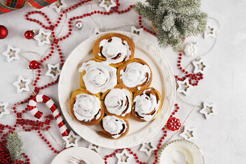 Christmas tree shape cinnamon rolls or cinnabon buns with cinnamon and cream sauce on white plate and christmas background. Festive idea for Homemade winter festive dessert buns pastry. Top view.