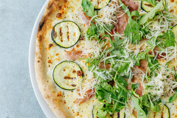 Fresh artisan pizza on a bright background with fresh rucola and ham