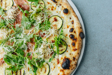 Fresh artisan pizza on a bright background with fresh rucola and ham