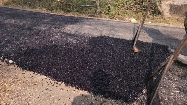 Close-up view of a worker leveling freshly laid bitumen with a rake during road construction, showcasing infrastructure development in a village area.