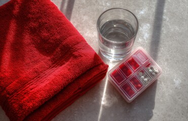 Pill organizer and water glass beside folded red towel