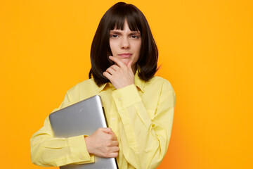 Obraz premium Thoughtful professional holds a laptop against a bright orange backdrop, conveying focus, modern productivity, and calm preparation in a bold daily work scene.