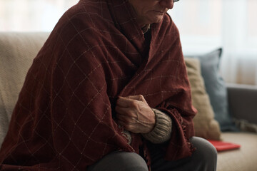 Senior Caucasian man sitting on sofa wrapping himself in blanket, while being sick with cold or...