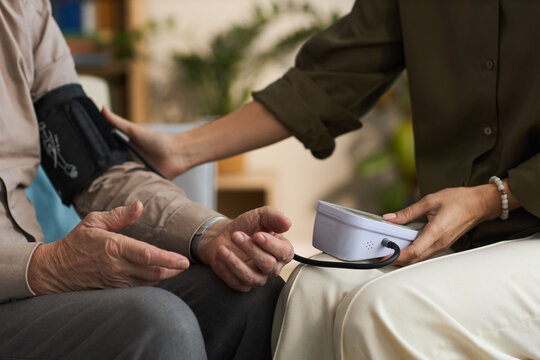 Caucasian senior man sitting while young adult woman measuring blood pressure using digital monitor, hands and partial arms visible, focus on healthcare interaction