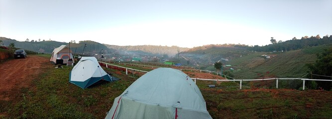 A young woman rests on a bench near her tent while camping in the lush green forest during winter in Phu Hin Rong Kla National Park, Phu Lom Lo.
