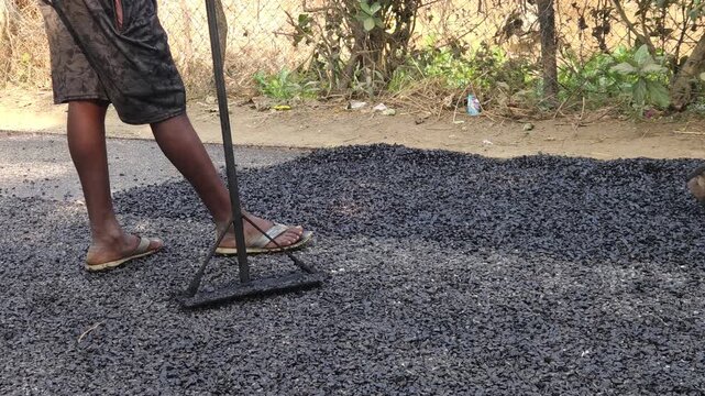 Construction worker manually spreads hot asphalt on a rural road using traditional tools, highlighting labor-intensive road construction practices in India.
