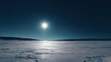 Bright sun shines over a frozen landscape with mountains in the distance under a clear sky