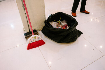 Red broom, dustpan, and full trash bag on clean tiled floor
