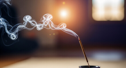 A close-up of a burning incense stick with elegant swirls of white smoke rising against a dark, warm background. A soft bokeh light source adds a meditative and spiritual feel