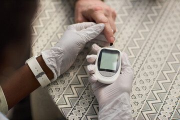 Caucasian senior hand being tested by Black woman using blood glucose meter, healthcare worker...