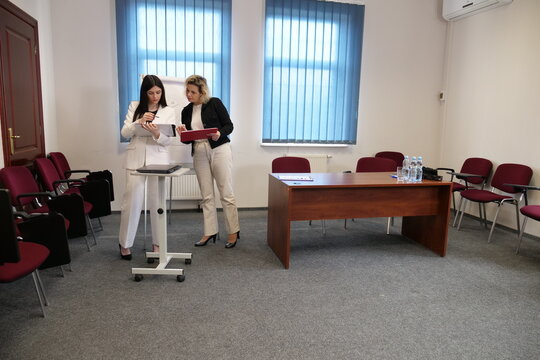 Two businesswomen discussing data on tablet near flip chart - Powered by Adobe