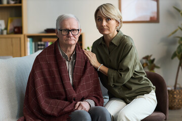 Portrait of senior Caucasian man sitting with blanket over shoulders, middle aged Caucasian woman...