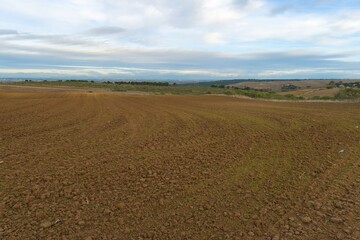 Farm field is prepared for planting crops in a rural area on a cloudy day with distant hills in sight