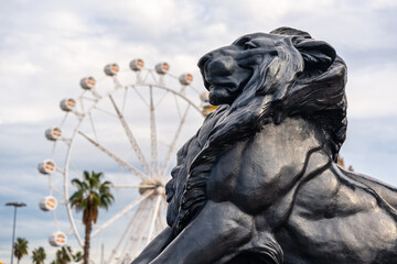 Lion statue in Columbus Square with the Ferris wheel in the background by the sea, Barcelona.