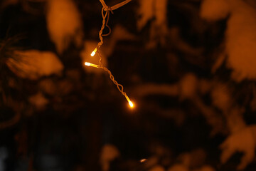 Warm glowing string lights hanging from a snowy branch, creating a cozy atmosphere in a winter wonderland, illuminating the serene night scene with soft orange hues