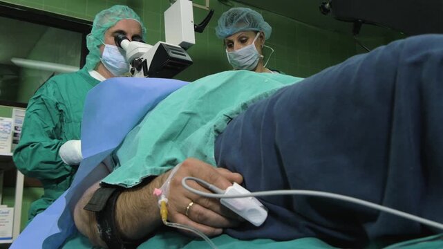 Surgeon and nurse performing cataract surgery on a male patient under anesthesia in operating room.