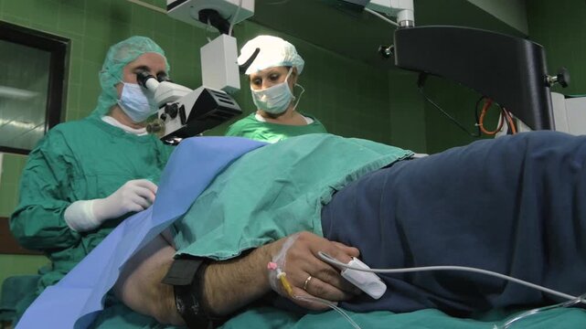 Surgeon and assistant performing cataract surgery on a male patient in a modern high-tech operating room.