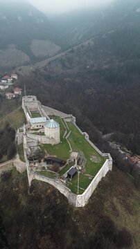 Aerial view of Travnik Fortress overlooking the town and surrounding hills, showing historic stone walls, green courtyards and misty mountain landscape from above. Amazing Bosnia and Herzegovina