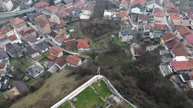 Aerial view of Travnik town with dense residential houses, narrow streets, and green areas surrounding historic walls, showing everyday urban life and landscape from above