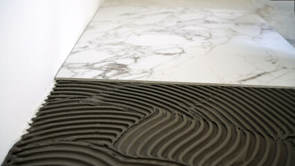 Worker applying adhesive mortar with a trowel for laying white marble pattern ceramic tiles during home renovation project