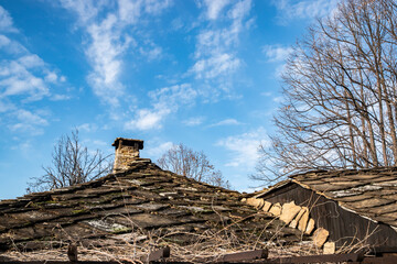 Traditional rural house roof with stone chimney and layered stone tiles under clear blue winter sky