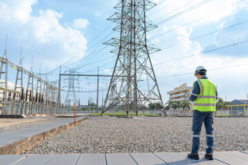 Electrical engineer in safety vest standing at power substation, monitoring high voltage...