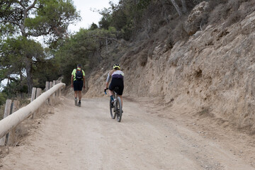 People enjoying outdoor activity on a gravel path along a hilly coastal environment, promoting fitness and adventure