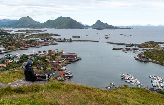 Woman Hiker enjoying panoramic view of ballstad village, traditional red houses, boats, and surrounding mountains in lofoten islands, norway