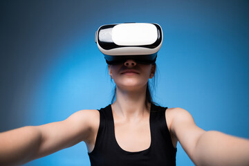Young woman wearing virtual reality headset and reaching forward, immersive digital technology experience, futuristic VR interaction concept on blue background