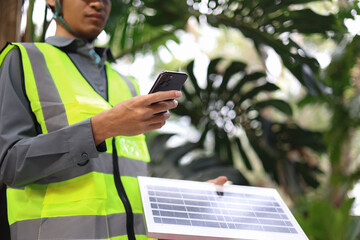 man wearing a high-visibility safety vest and a hard hat, checking operation of&nbsp;solar panel&nbsp;system with digital tablet or smartphone.