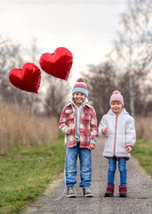 smiling kids couple walking together with two red heart balloons 