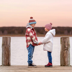 romantic children couple standing on the wooden pier and holding their hands