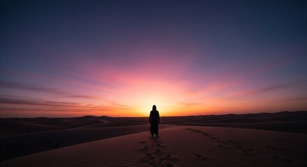 Obraz premium Silhouette of a person walking on a sand dune at sunset, with colorful sky and footprints