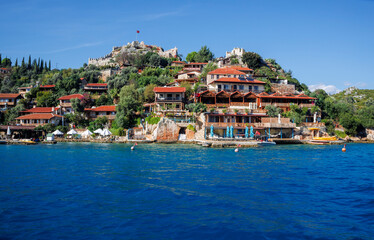 Fototapeta premium Picturesque Turkish coastal village with a striking white mosque featuring a green-topped minaret rising above terracotta-roofed houses along a serene waterfront. 