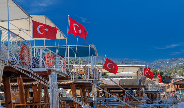 Panoramic wooden pier walkway lined with traditional Turkish gulets and boats flying red flags in a turquoise marina bay. Serene summer scene with green hills and blue skies,