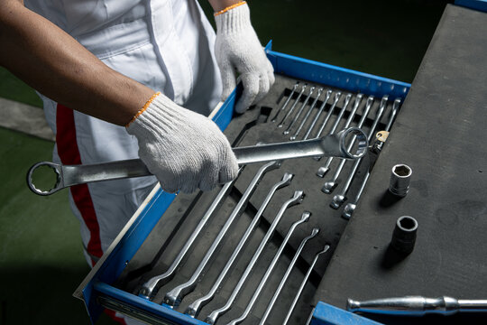 Mechanic hand picking up a wrench from a professional tool chest drawer.  
Close-up of a technician in white uniform selecting a chrome wrench from an organized toolbox. Highlighting workplace 