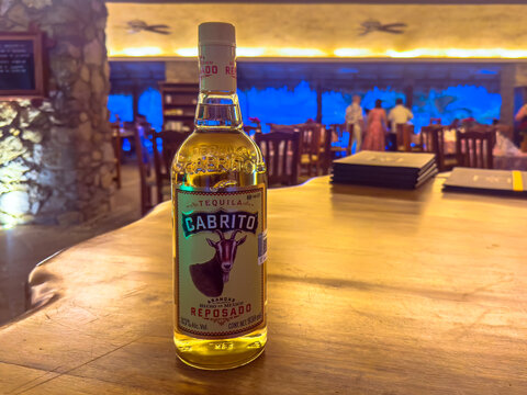 Huatulco, Oaxaca, Mexico. Dec 31, 2025. Close-up of a Tequila Cabrito bottle on a rustic wooden table with a blurred restaurant interior and diners in the background.