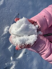 A girl in pink gloves in a snowy park holds white fluffy snow in her hands