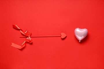 Composition with cupid's arrow and air balloon in shape of heart on red background. Valentine's Day celebration