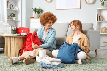 Redhead mother with her teenage daughter packing emergency backpacks at home