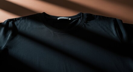 Fototapeta premium Black t-shirt laid flat with soft sunlight and diagonal shadow lines across fabric