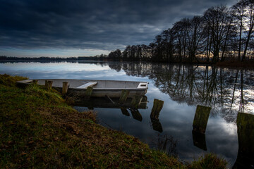 Empty boat on calm lake with dark dramatic sky and reflections