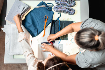 Top view of two fashion designers collaborating on a clothing project with fabric swatches and patterns in a creative studio.