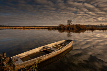 Obraz premium Abandoned wooden boat on calm lake with dramatic cloud reflections